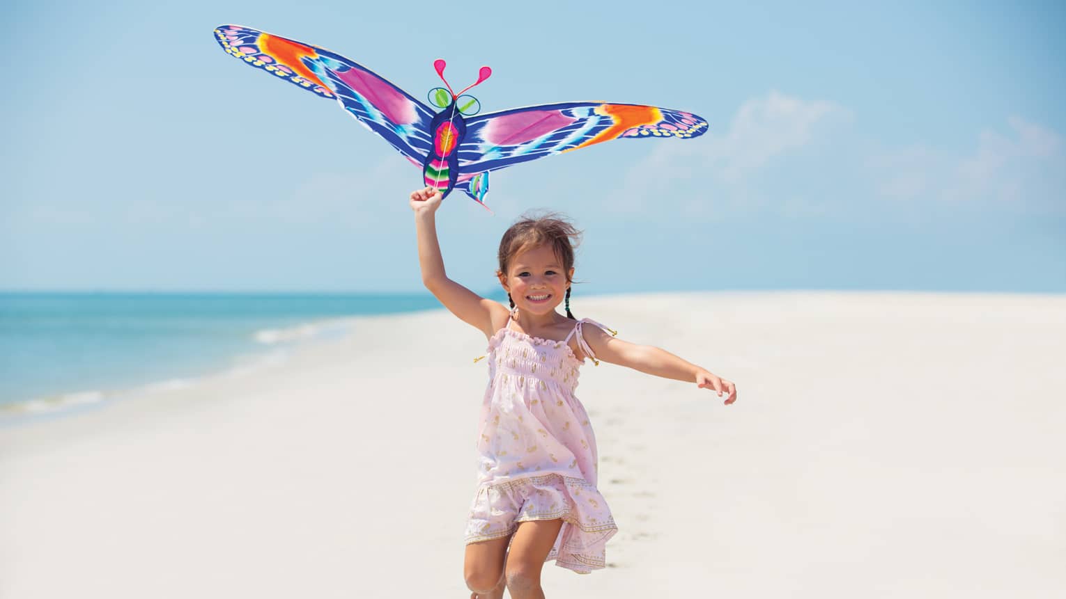 Young girl runs with colourful butterfly kite on white sand beach