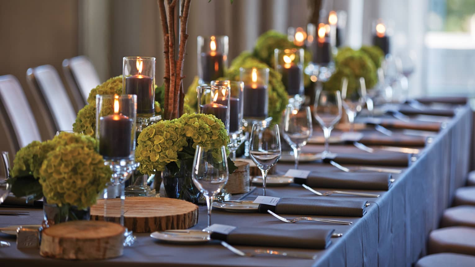 Black pillar candles in votives, green flowers, wine glasses along banquet table