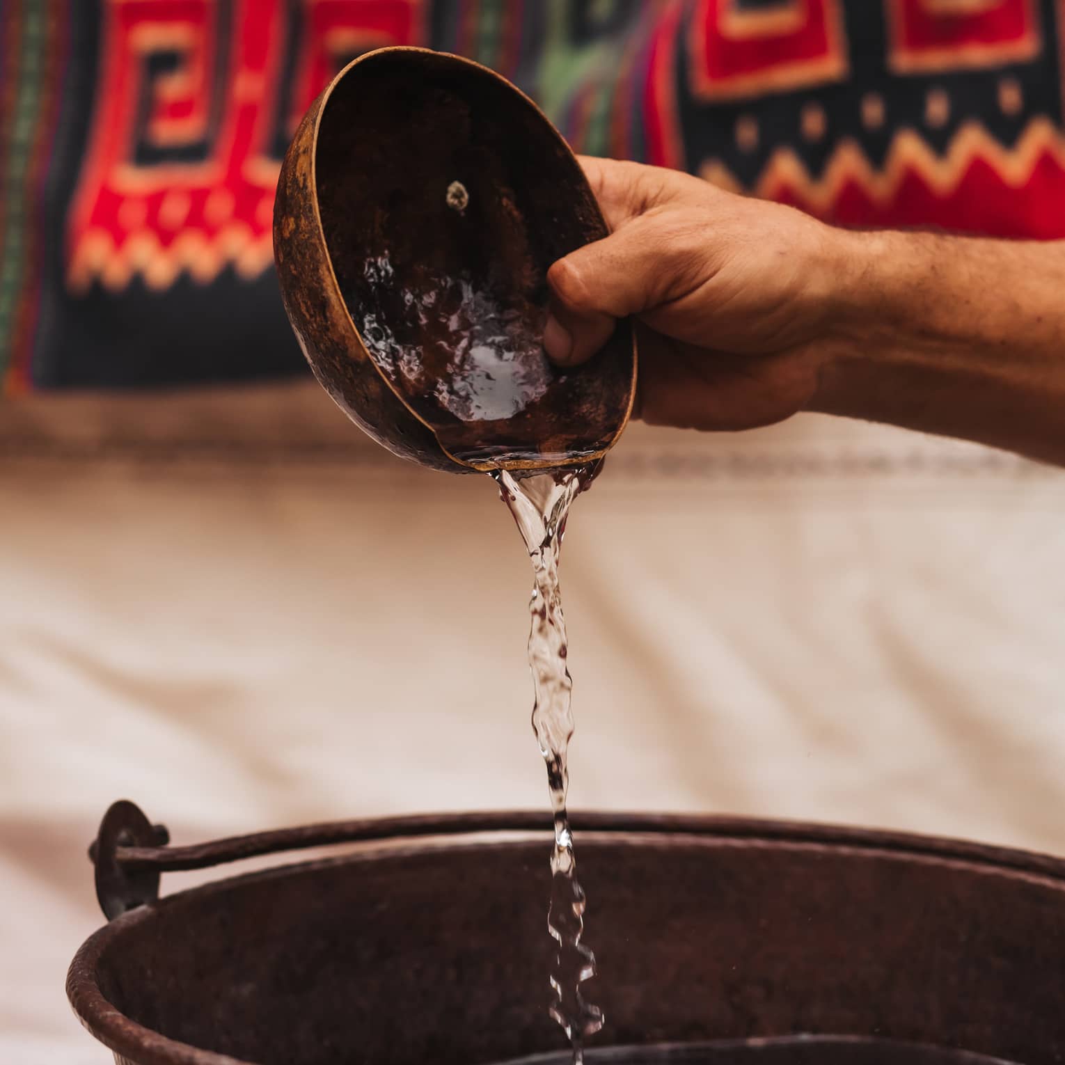 Hand pours water from coconut shell into bucket beneath