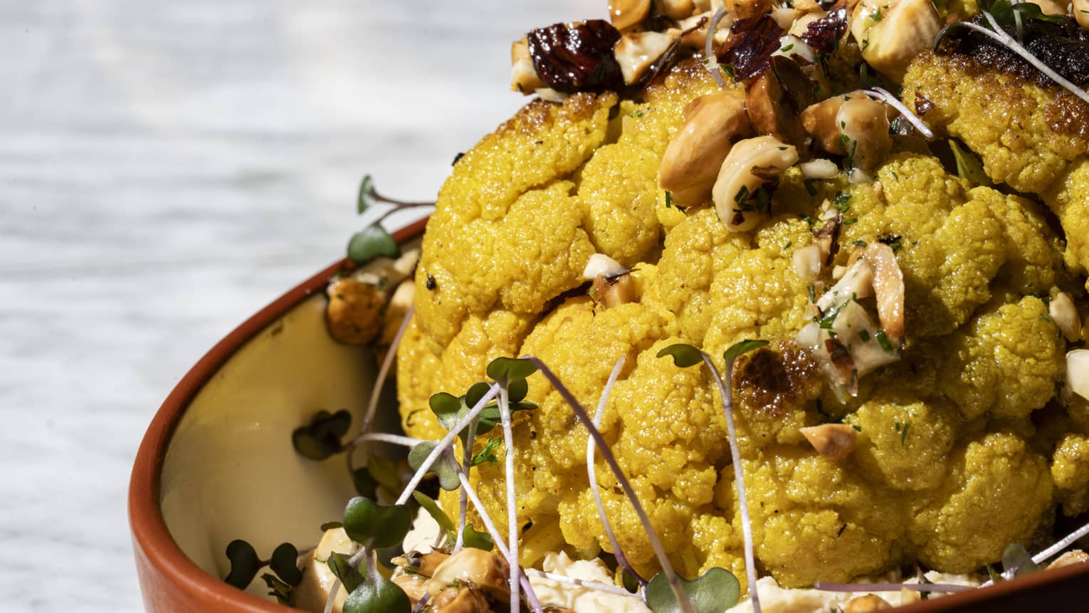 Curried cauliflower topped with garnish and served in a red stoneware bowl