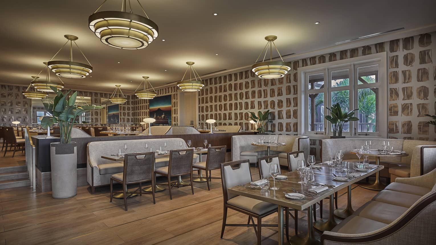 A dimly lit interior of a dining outlet with wood floors, large chandeliers and cushioned booths.