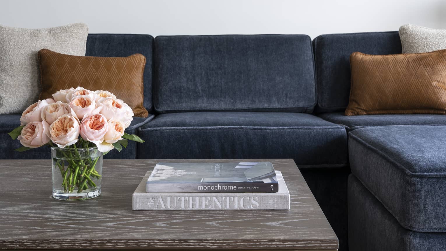A blue couch near a grey coffee table with books and flowers on it.