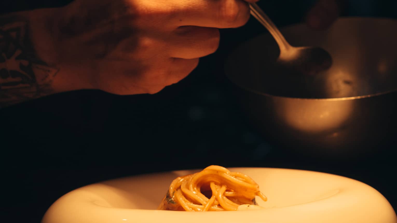 Person scooping noodles from one bowl into another.