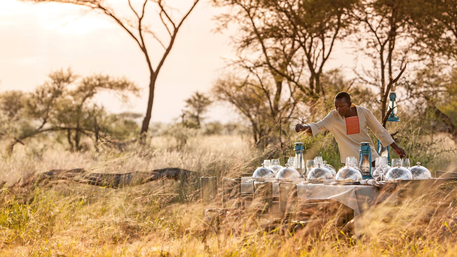 Hotel staff places lantern on long dining table with silver dome planets in grassy field