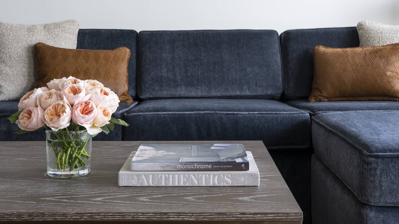 A blue couch near a grey coffee table with books and flowers on it.