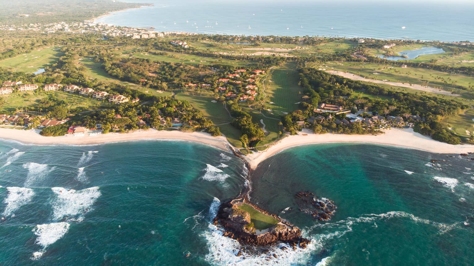 A coastline with deep blue water running up against sand and plants.