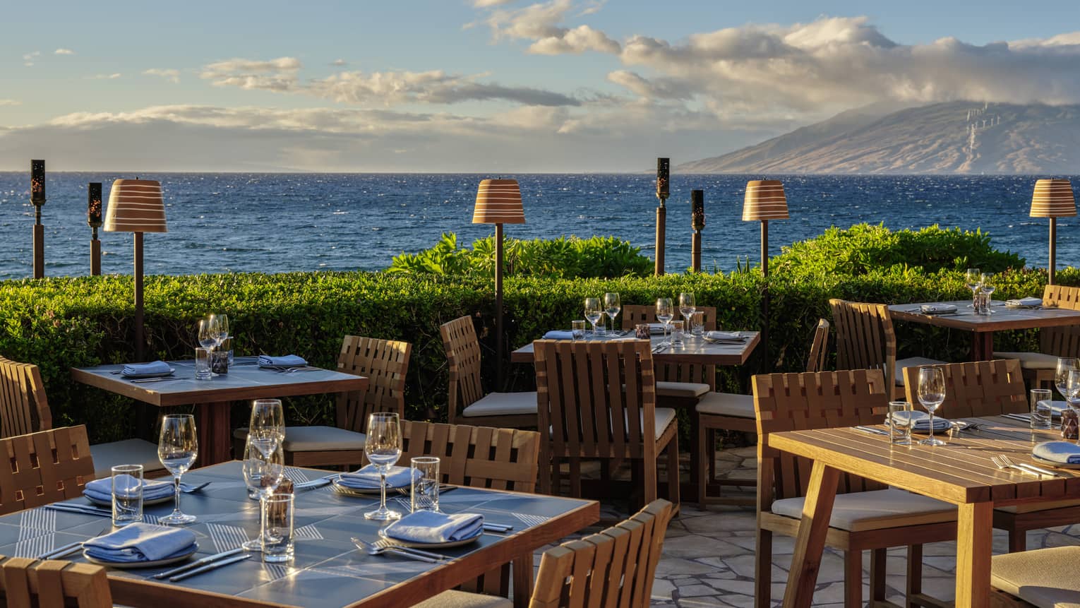 Oceanfront outdoor dining area with wooden tables and chairs set for service