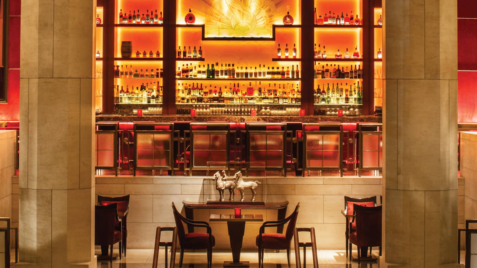Yellow, amber lights on liquor display behind Art-Deco style bar between stone pillars