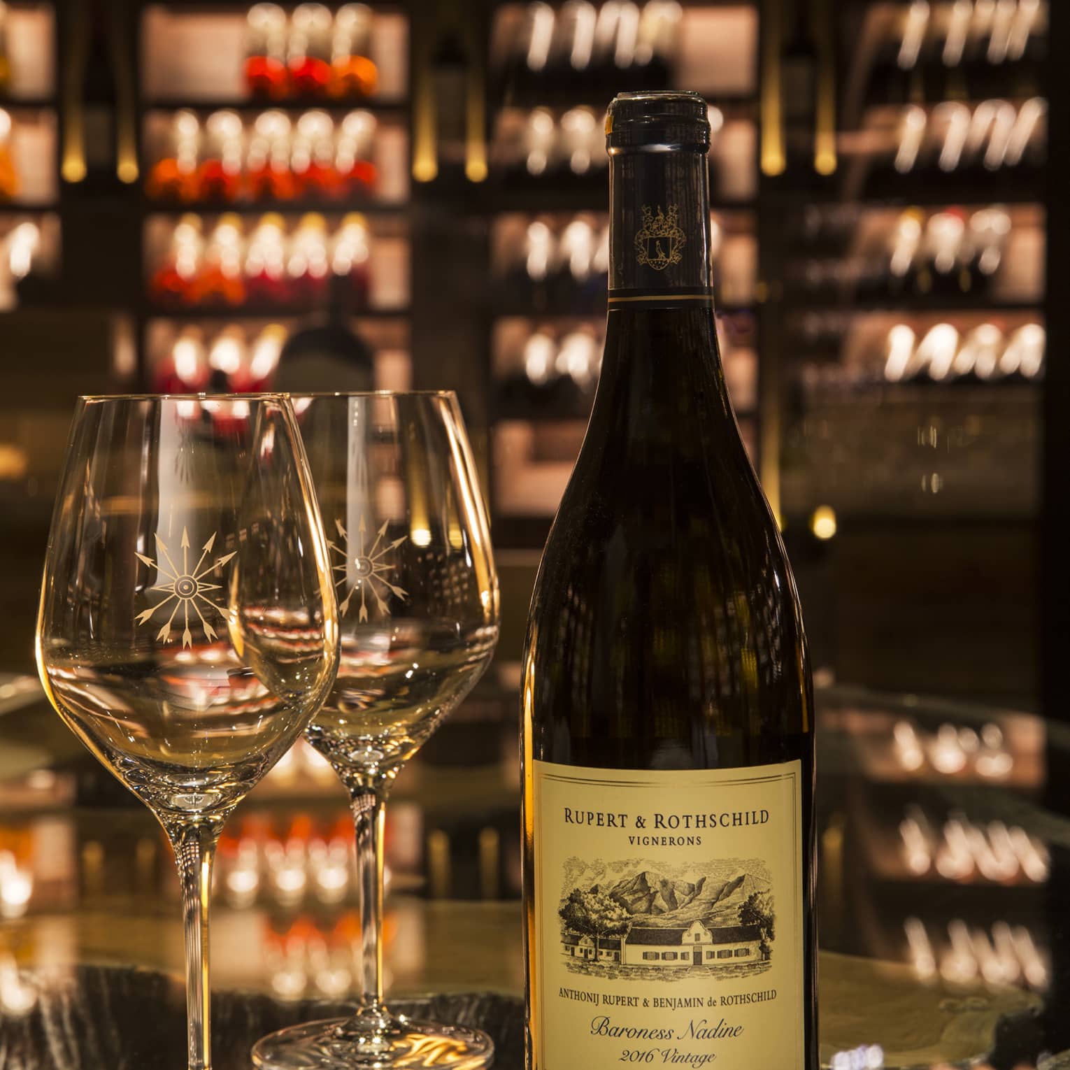 A close-up of two sparkling wineglasses and a dark bottle of sealed Rupert & Rothschild wine.