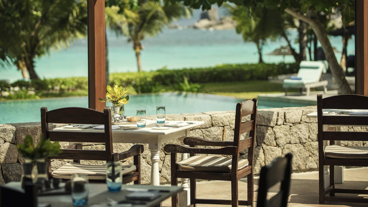 Outdoor dining table and chairs overlooking pool with tropical foliage