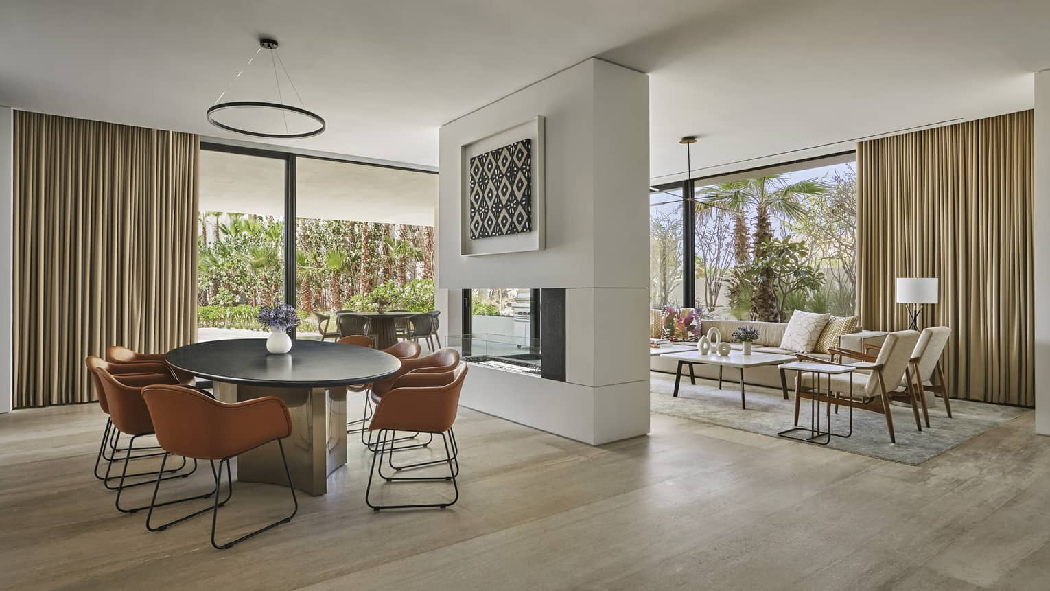 Dining room with oval table and four modern leather chairs, fireplace wall separating living room