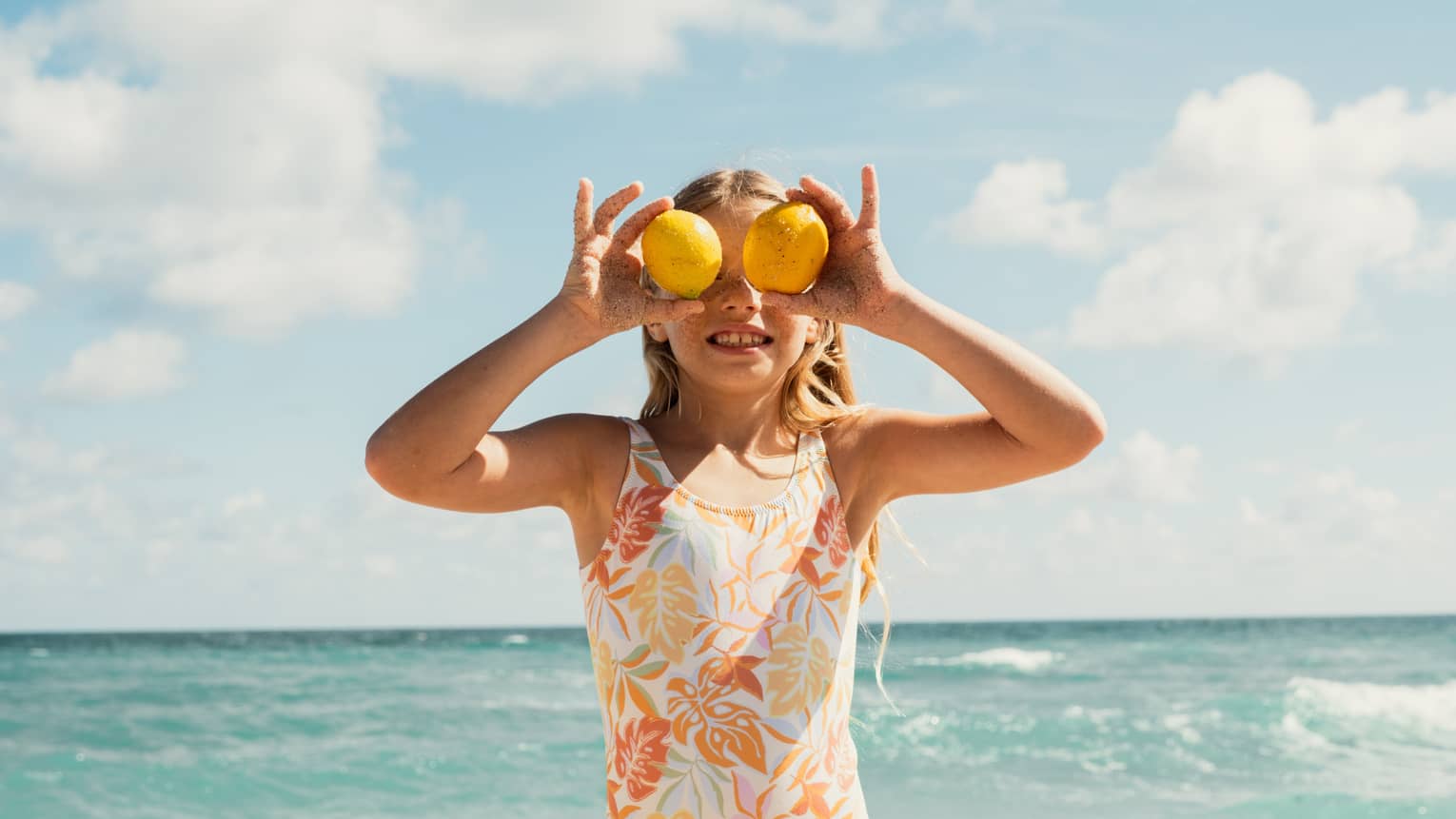 Girl holding two lemons over her eyes on a beach