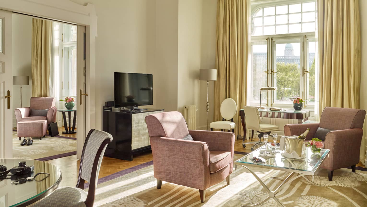 Chain Bridge Suite room with pink armchairs, glass coffee table, desk in front of large sunny window, yellow curtains