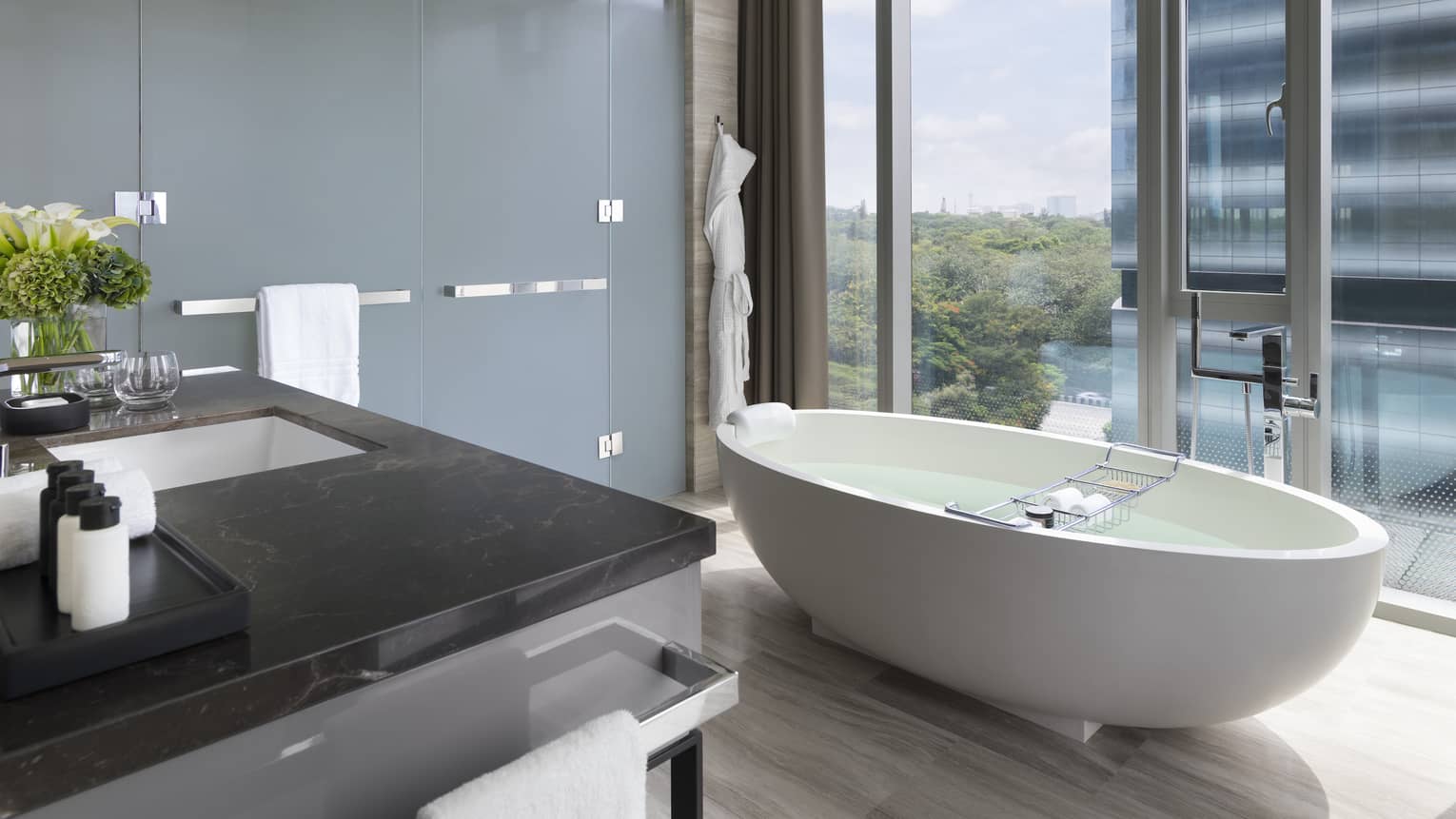 Bathroom with white free-standing tub set next to a floor-to-ceiling window