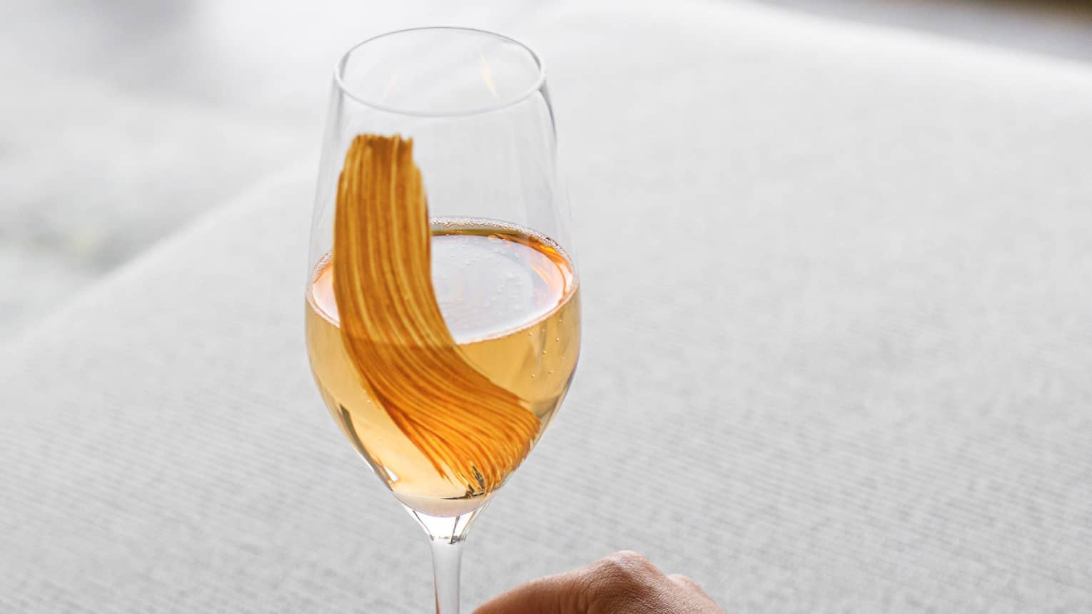 Hand holding Andromeda cocktail of Sancerre Rose Liqueur, Brut Champagne in tall crystal wine glass