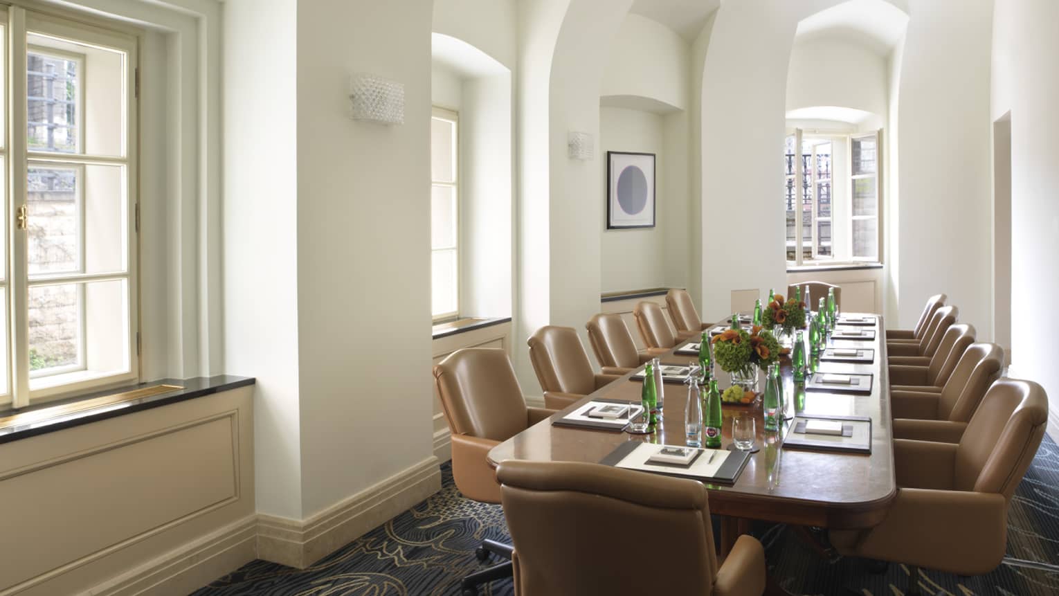 Sunny meeting room with large boardroom table lined with tan executive chairs