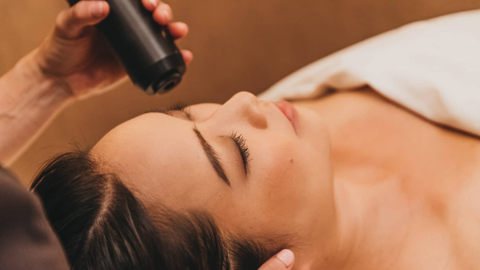 A spa staff member applies a cryotherapy treatment to a woman's forehead