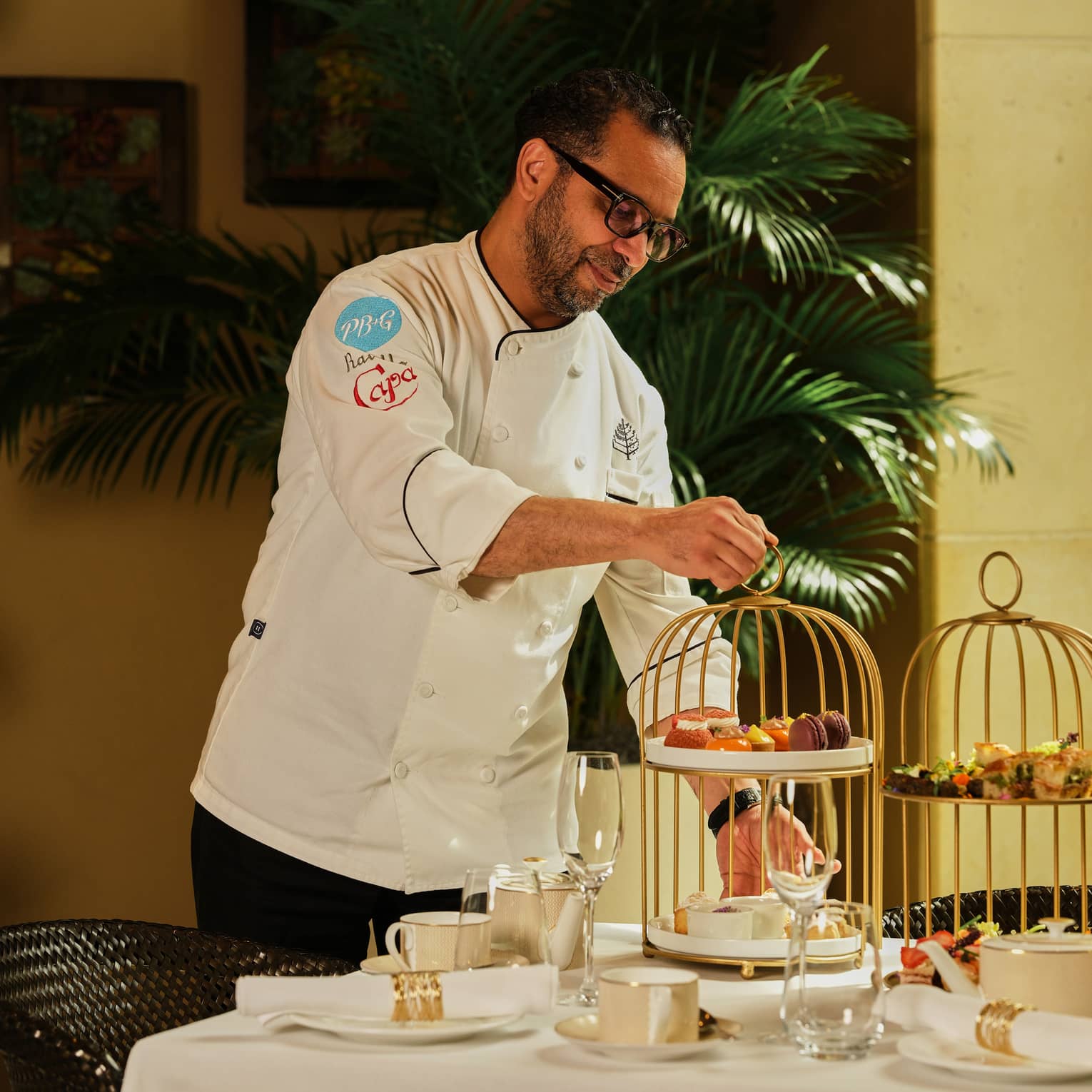Chef places a tiered tray of pastries onto a table set for afternoon tea