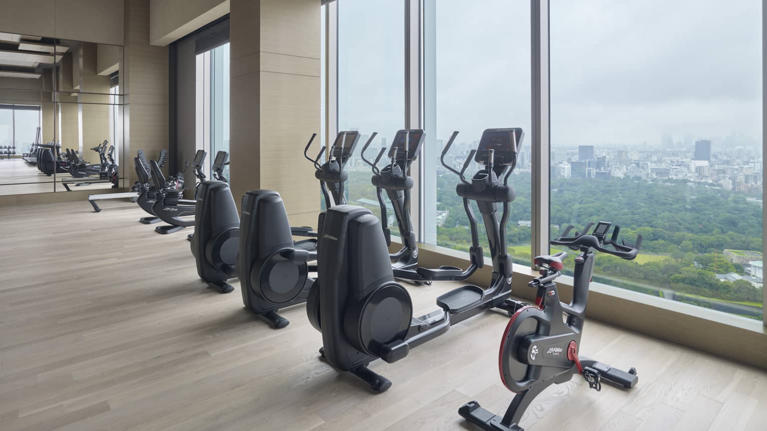 Row of fitness equipment in front of floor-to-ceiling windows with views of the city 