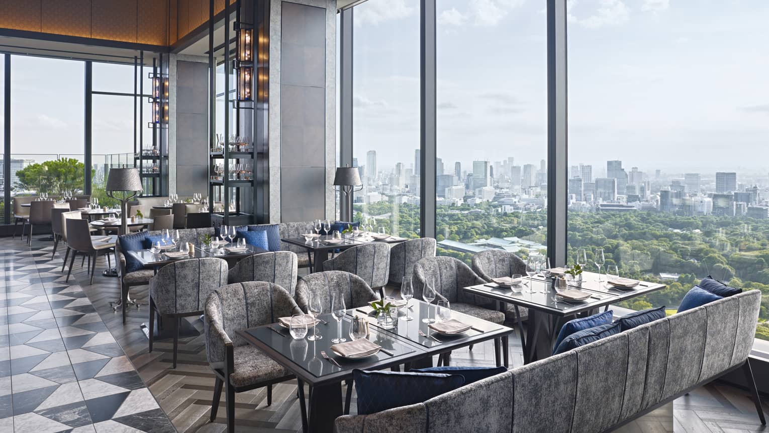 Restaurant with square tables and grey chairs/sofas, black-and-white tile floor, wall of windows looking out to Imperial Gardens in Tokyo