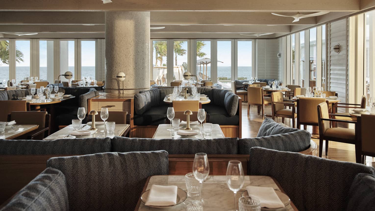 The interior of a restaurant with large booths, large windows, fans and wood fixtures.