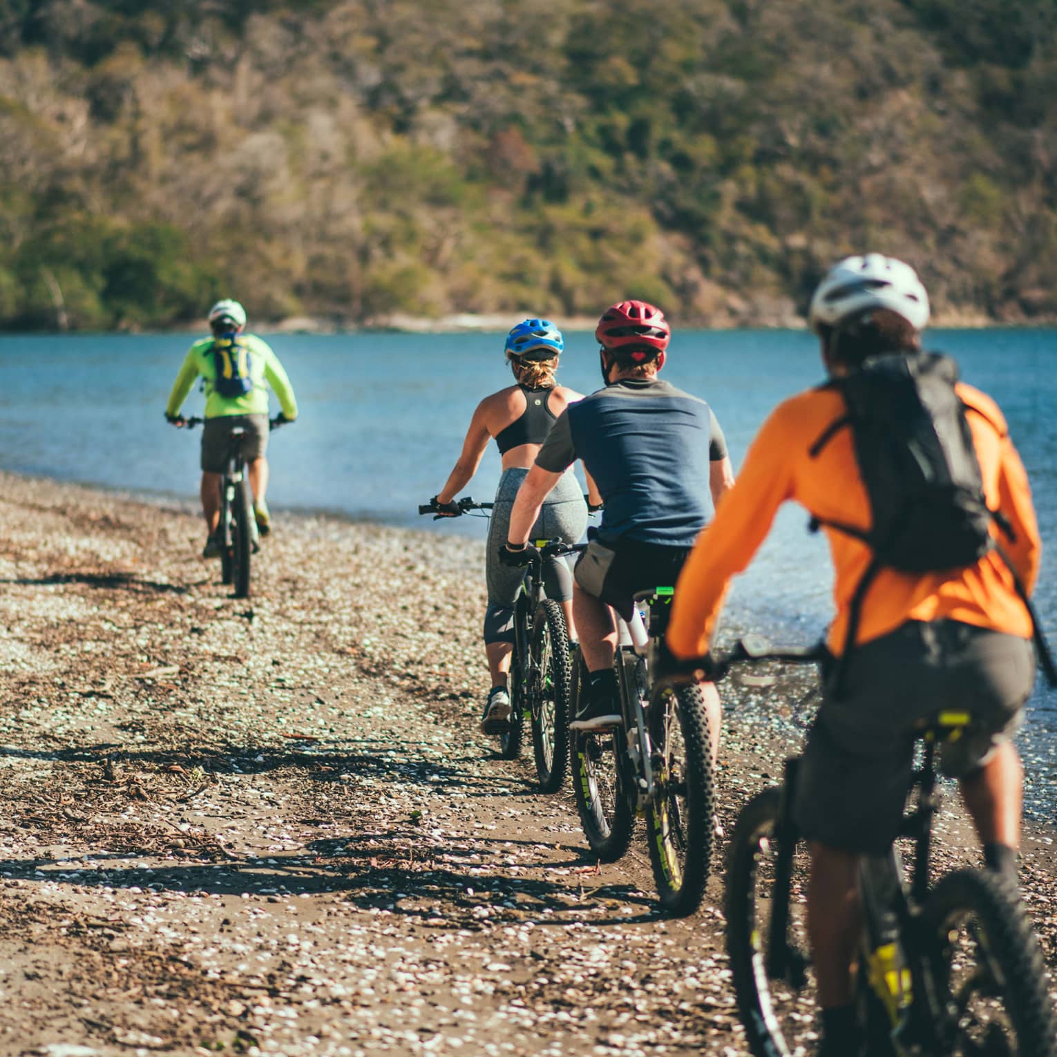 Four people riding bicycles through a rocky terrain next to the ocean