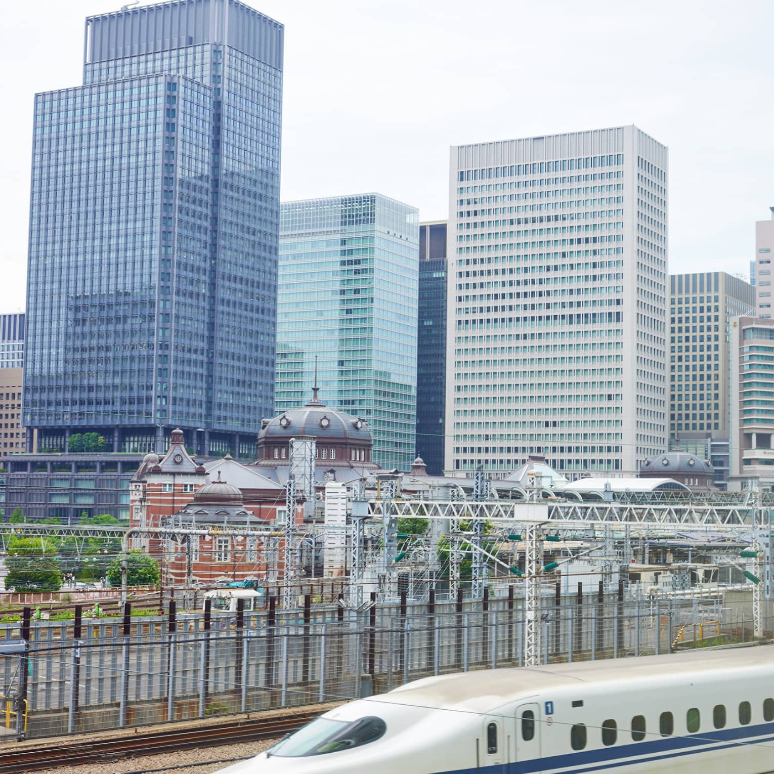 The Shinkansen bullet train speeds past Tokyo's railway station dwarfed by the skyline of rectangular, glass high-rises.