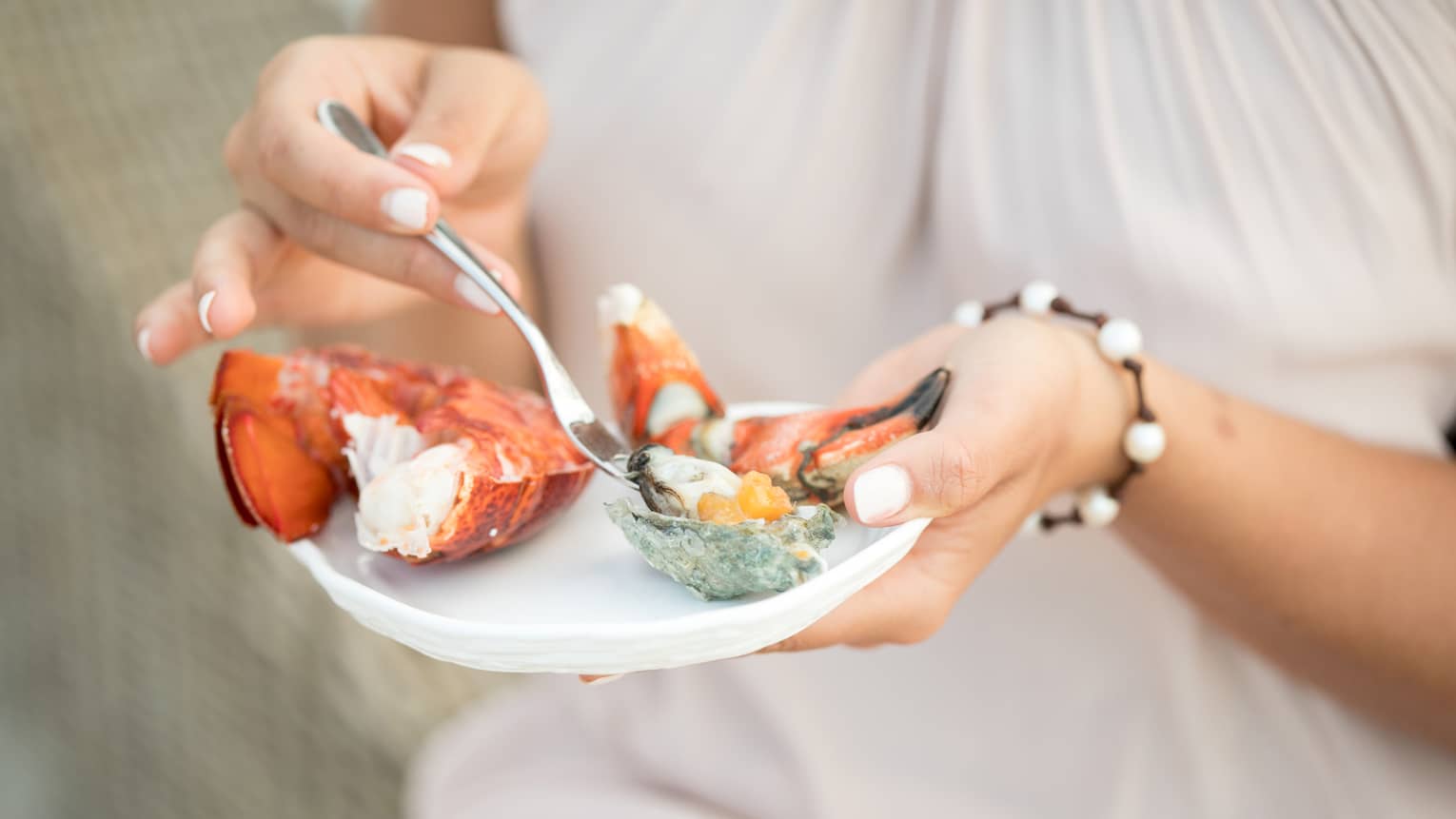 Close-up of woman holding small plate with fresh seafood, digging fork into oyster