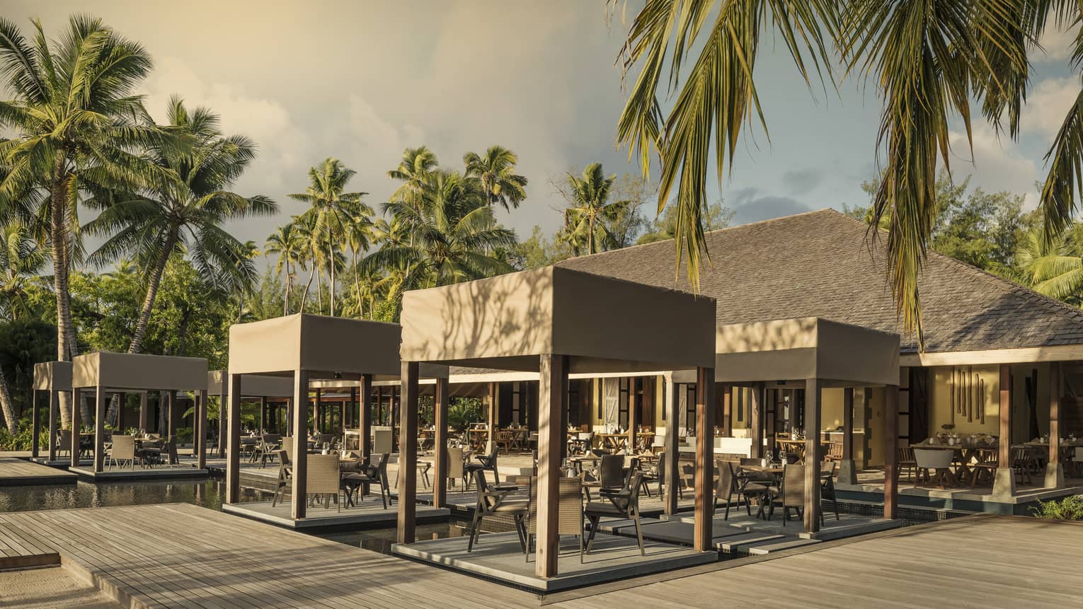Outdoor Claudine restaurant with tables on decks over water, covered with wooden canopy
