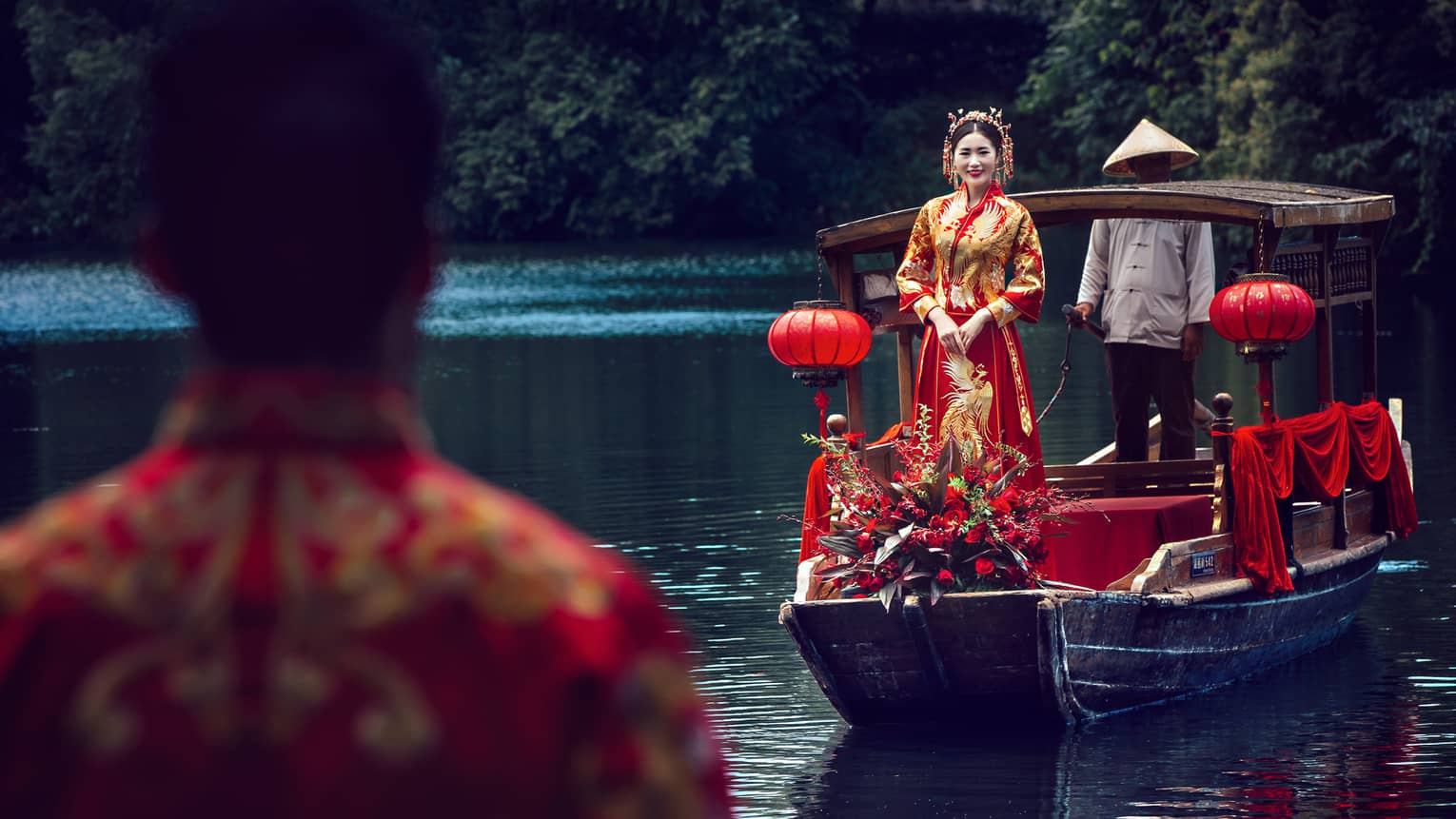 Boat leads bride wearing traditional dress towards land where groom waits