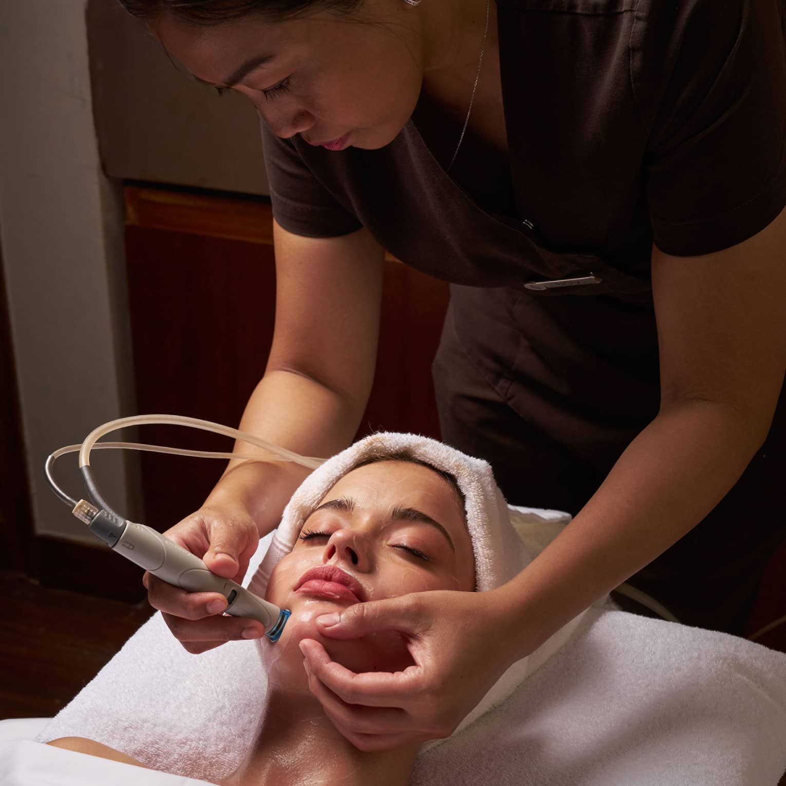 Spa therapist performs facial on female guest with tool