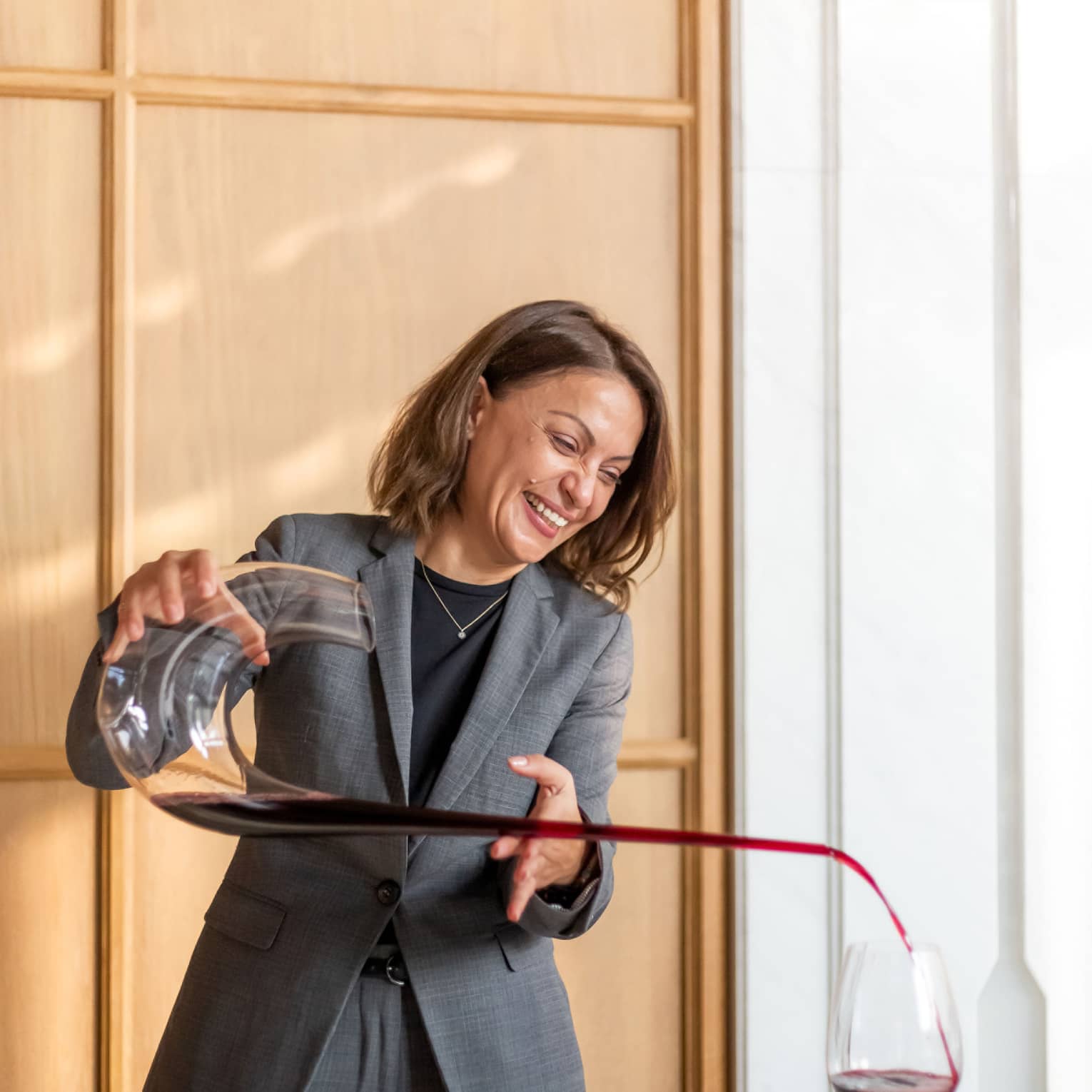 Brasserie Palmier Bar sommelier smiles, pours red wine from long decanter into wine glass on table