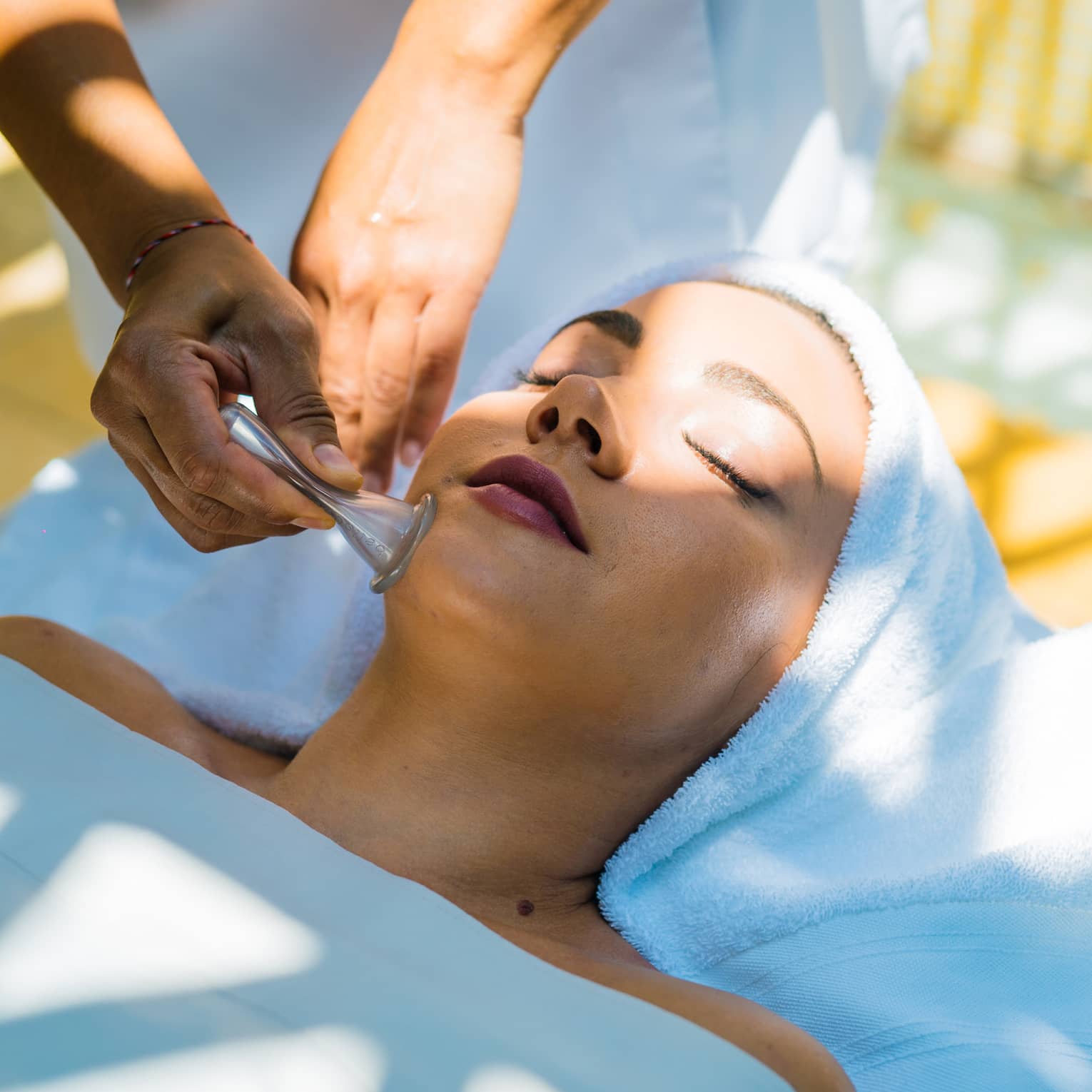 A woman lays on a table as a masseuse uses a roller on her face.