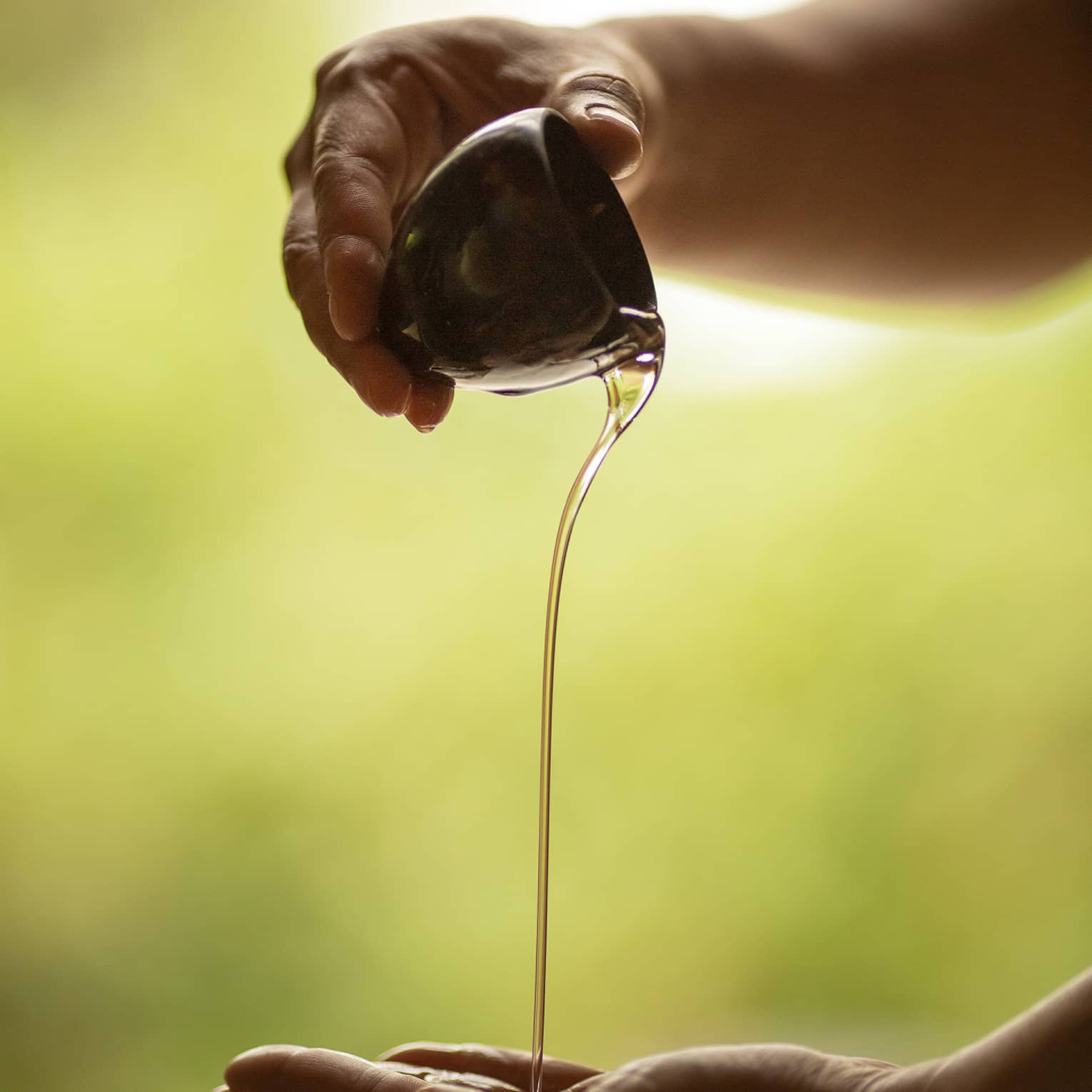 A set of hands pours massage oil from a ceramic bowl into a palm