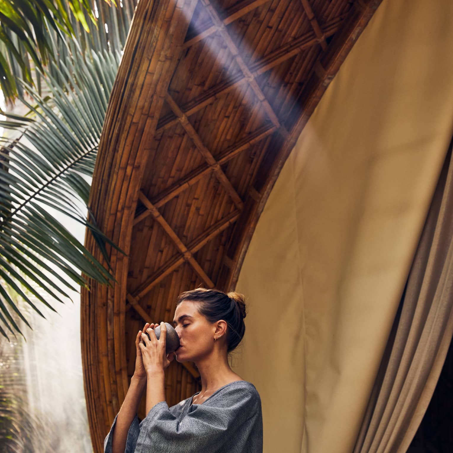 A woman drinking near palm trees and a large spa pod.