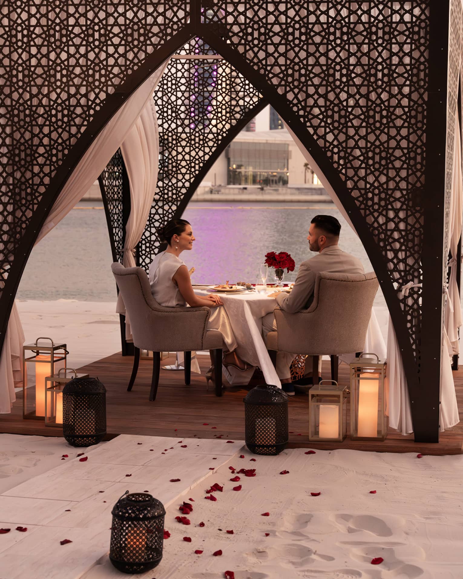 A couple dines in a beach cabana adorned with Arabian-style arches, candle lanters and rose petals along the walkway leading to the cabana