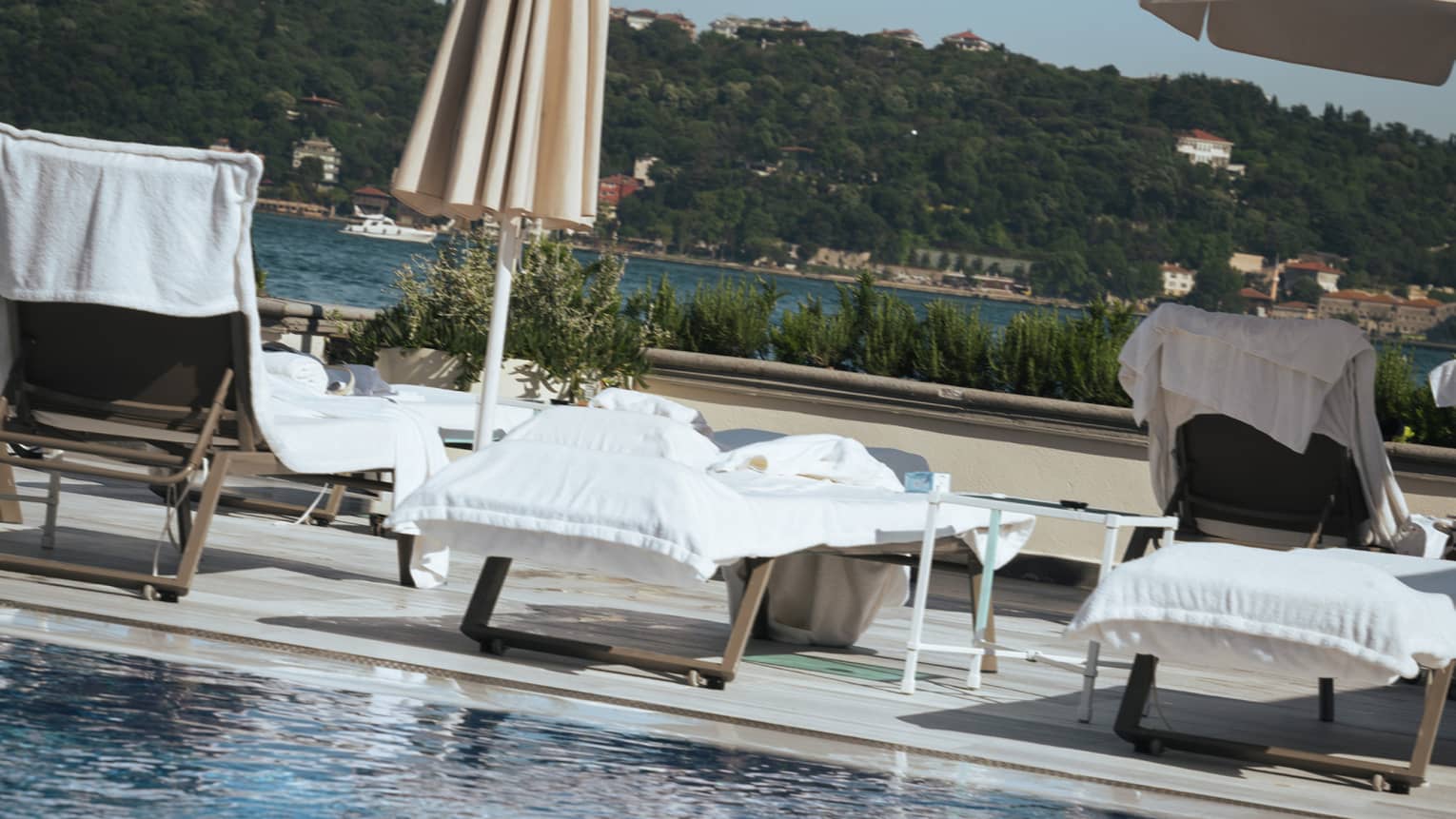 A person in a bathing suit and sunglasses at the edge of a clear blue pool. Lounge chairs, umbrellas and the distant landscape are in the background