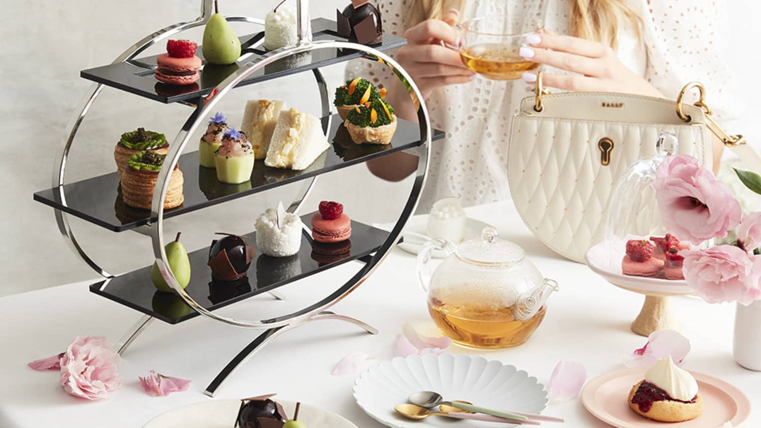 Woman enjoys afternoon tea, a three-tiered array of desserts in front of her