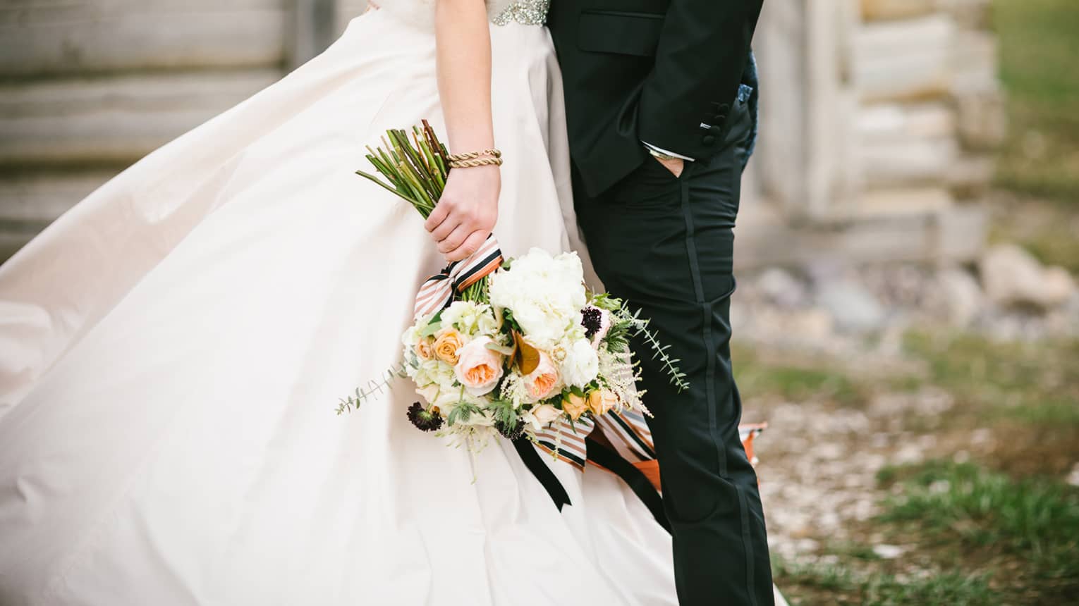 Close-up of a couple dressed in wedding attire, with one partner in a black suit and the other holding a bouquet of flowers