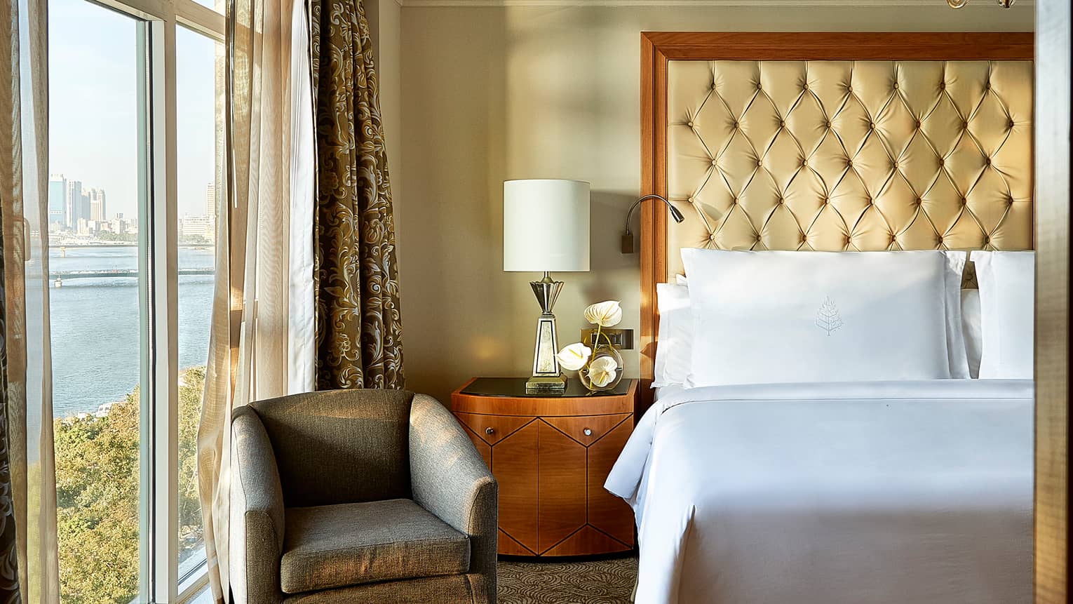 Royal Suite close-up of white pillows and tall leather headboard, wooden side table with lamp and white orchids