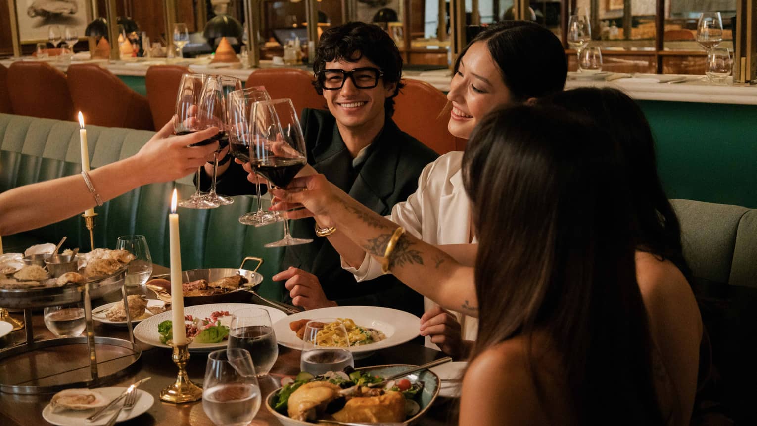 A group clinks glasses of red wine over a dining table filled with various vibrant culinary dishes