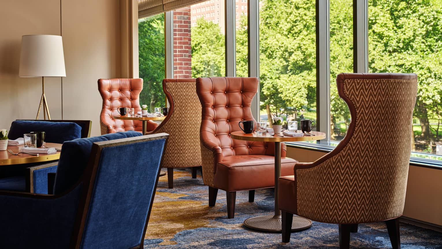 Dining room with tables and orange chairs next to the window and navy blue chairs beside the table in the middle of the room.