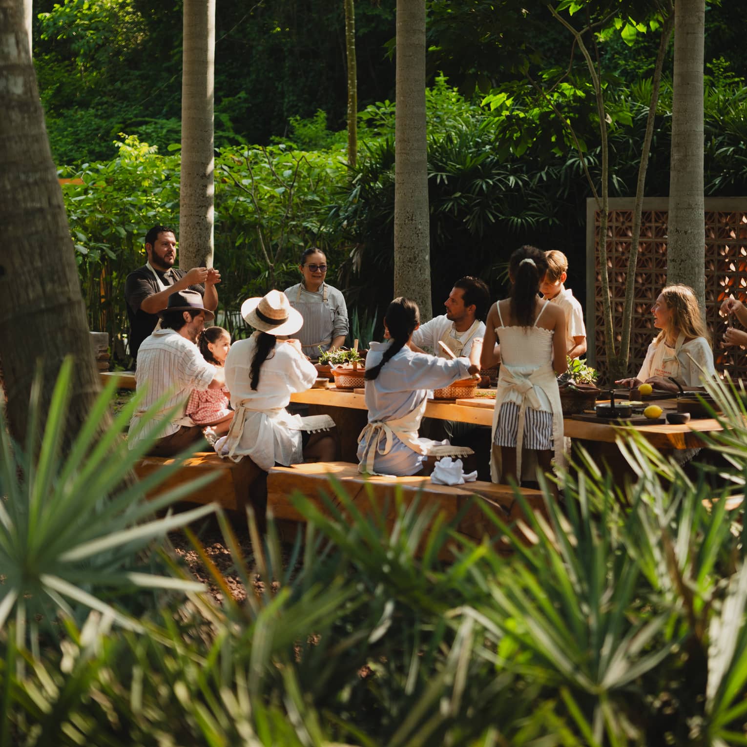 People seated around a long outdoor dining table set among palm trees