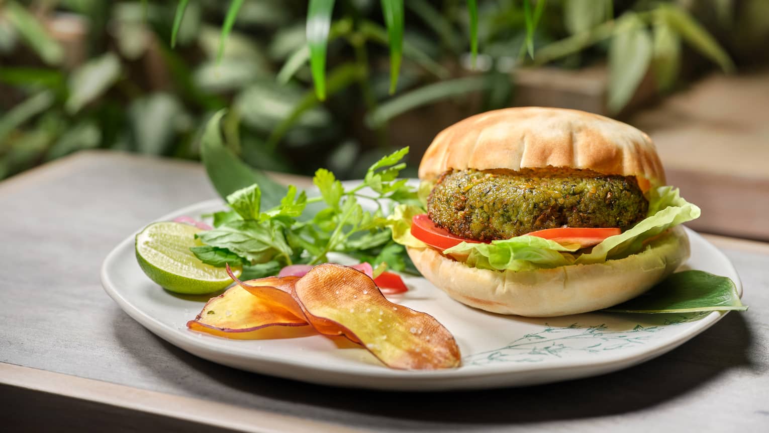 Green-hued vegetable burger with fresh herbs and lime cheek on round white plate