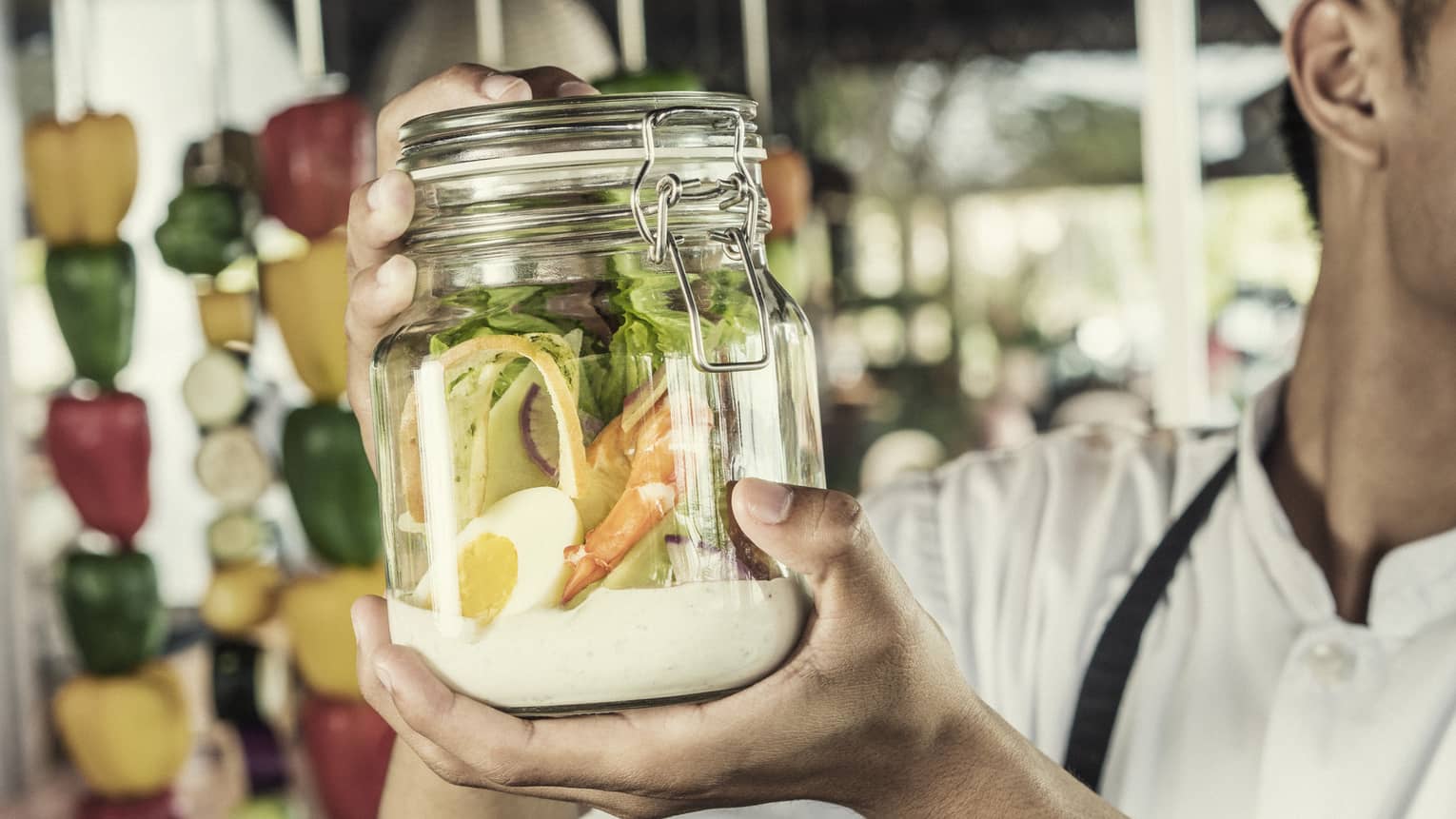 A chef shakes a caesar salad in a glass jar with some dressing