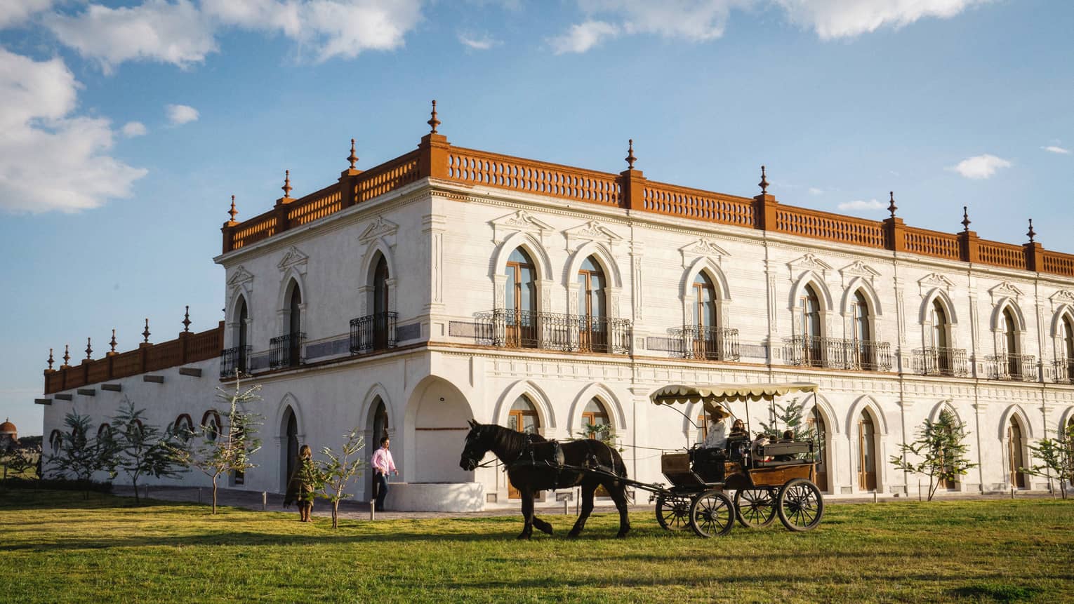 Guests enjoying a horse-drawn carriage ride around a large white building with several beautifully carved arched doorframes.