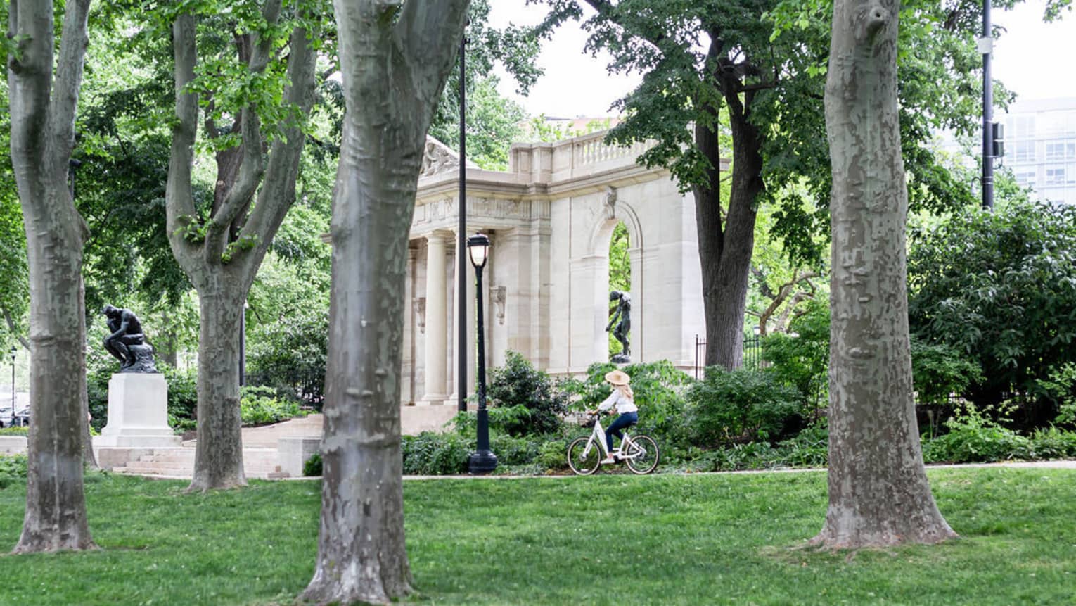 A person riding a bike through a park with trees and old stone architecture.
