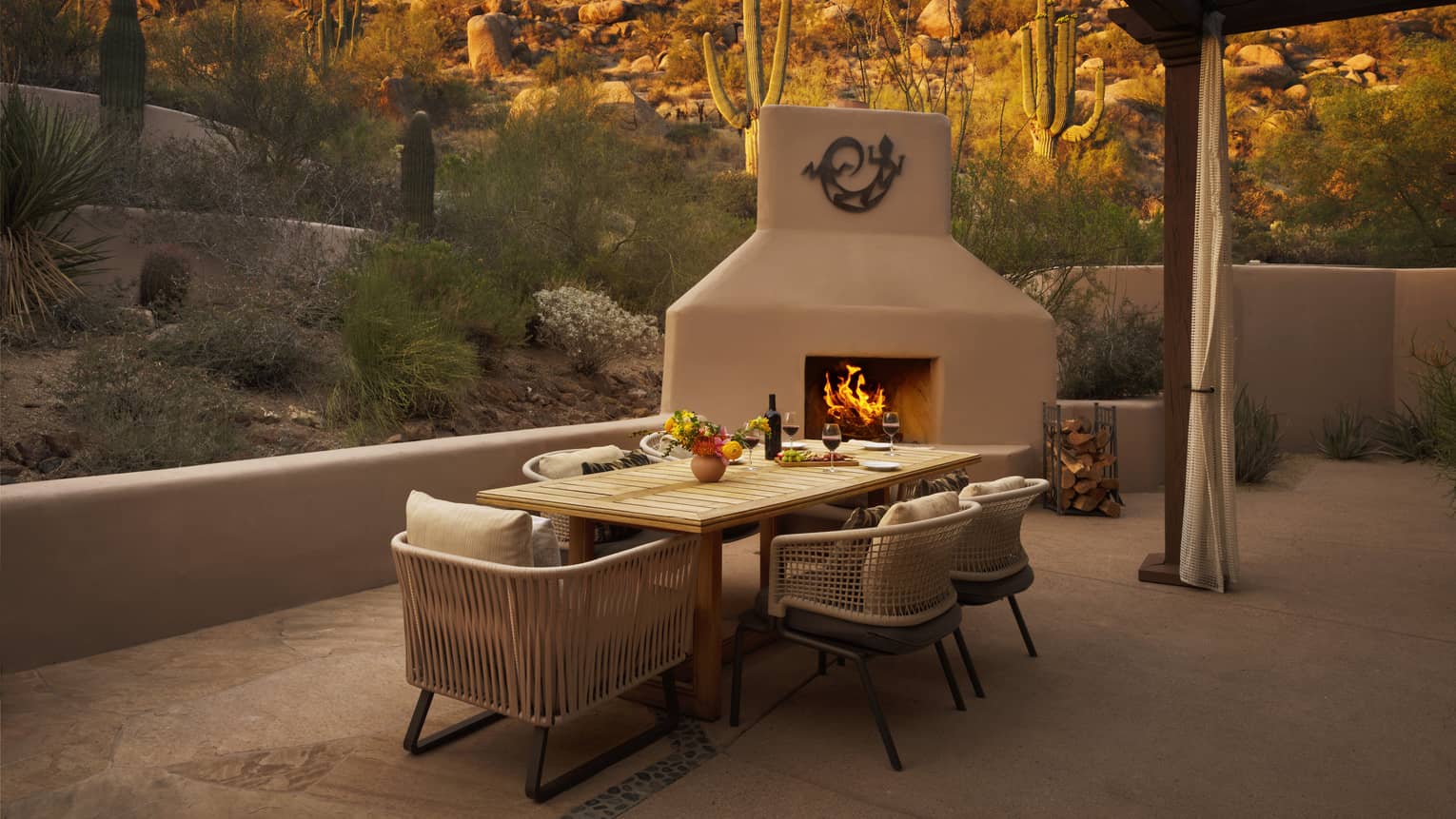Private terrace of a resort suite, featuring a contemporary dining table, outdoor fireplace and views of the desert and rocky mountain
