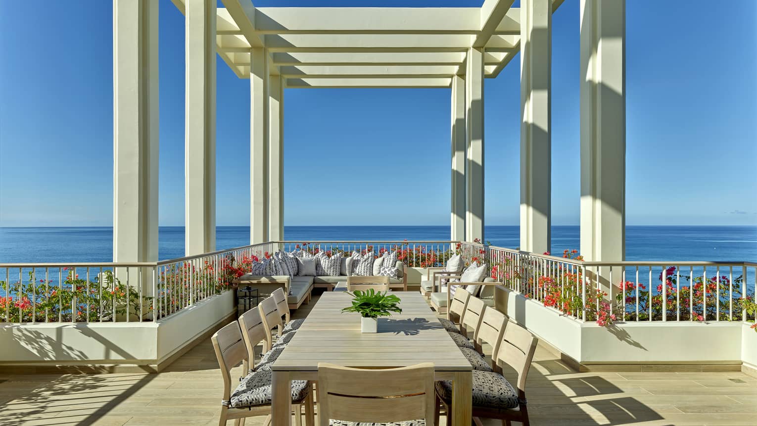 Ocean-view terrace with long dining table under pergola