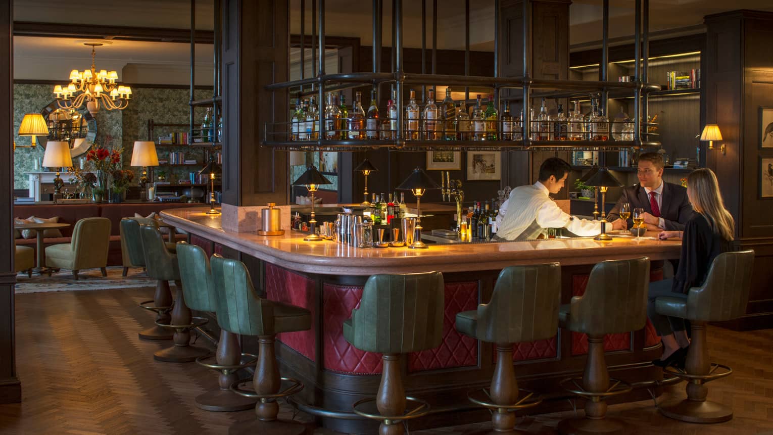 Bartender passes drink to couple on stools at rectangular bar in The Bar at Wild Carrot